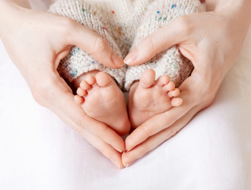 Mãe fazendo um coração com as mãos em volta dos pezinhos de um bebê